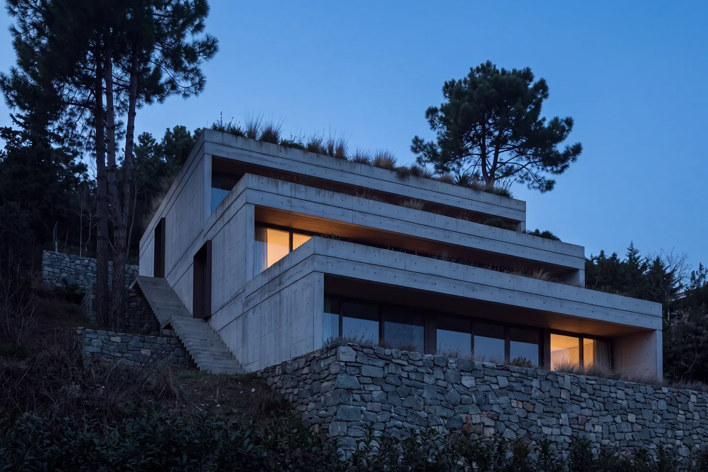 Alacakaranlıkta Kandilli Evi; yamaca karşı karanlık üç basamaklı terası, birkaç sıcak ışıklı açıklıkla.