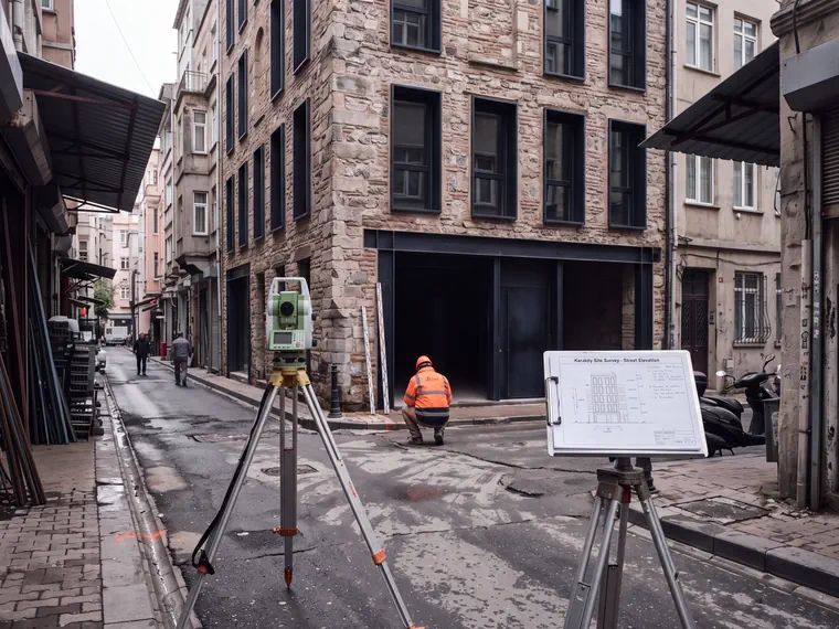 Karaköy Deposu'nun önündeki dar sokakta saha araştırması için kurulmuş, sehpa üzerinde bir total station ve bir stand üzerinde notlandırılmış sokak cephesi.